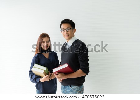 Asian male and female graduate students, wearing casual clothes, standing holding books and looking at the rear camera as a white background
