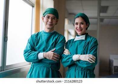 Asian Male And Female Surgeon Smiling To Camera After Finish Success Surgery. Medical Team Standing In Arms Crossed At Hospital.