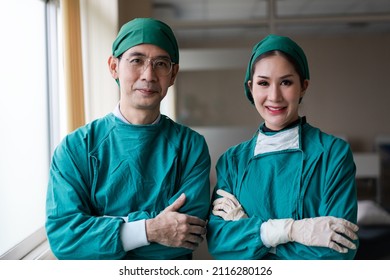 Asian Male And Female Surgeon Smiling To Camera After Finish Success Surgery. Medical Team Standing In Arms Crossed At Hospital.