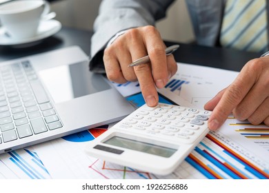 Asian male finance staff is calculating by using a calculator. Investment results to report to his boss at the meeting. On the table in the office, the concept of calculating investment results - Shutterstock ID 1926256886