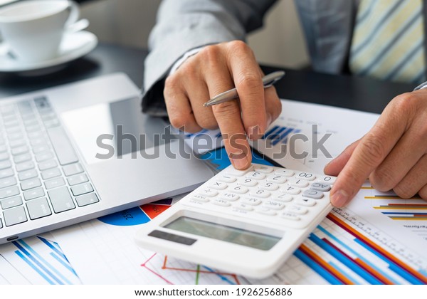 Asian male finance staff is calculating by using\
a calculator. Investment results to report to his boss at the\
meeting. On the table in the office, the concept of calculating\
investment results