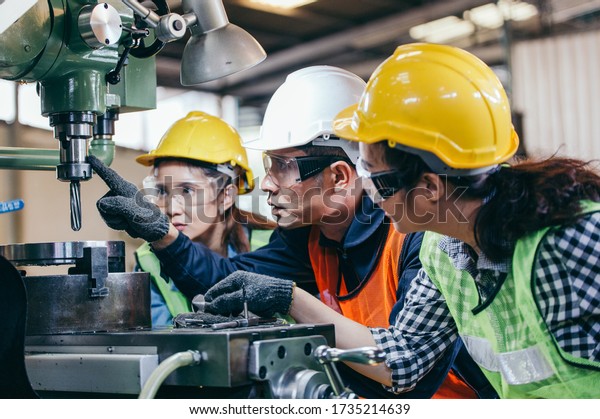 Asian male foreman manager showing case study of\
factory machine to two engineer trainee young woman in protective\
uniform. teamwork people training and working in industrial\
manufacturing business