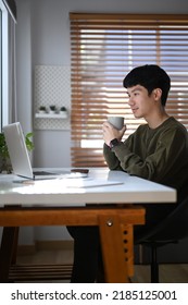 Asian Male Freelancer Drinking Coffee And Reading Online Information Or Email On Laptop Computer