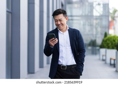 Asian Male Freelancer Walking Near Business Center Holding Phone, Smiling Reading News, Successful Businessman