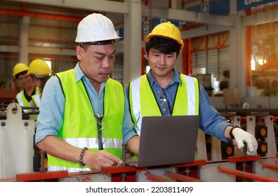 Asian Male Hard Hat Chief Engineer Uses Laptop To Train Workers To Check Checks Heavy Metal Machinery There Is A Team Working Behind The Scenes. Concepts, Factory Workers. Mechanical Engineering