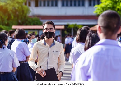 Asian Male High School Teacher Is Wearing A Mask And Standing Among Students In White Uniform During The Coronavirus 2019 (Covid-19) Epidemic.