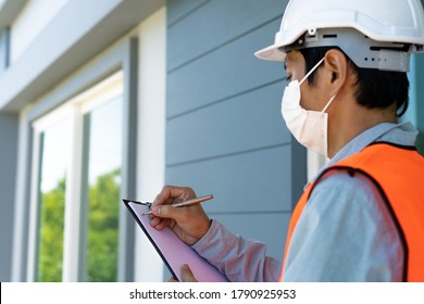 Asian Male Inspector Wearing A Mask And Safety Suit Is Taking Notes After Inspecting The Structure And Exterior Of The House Building.