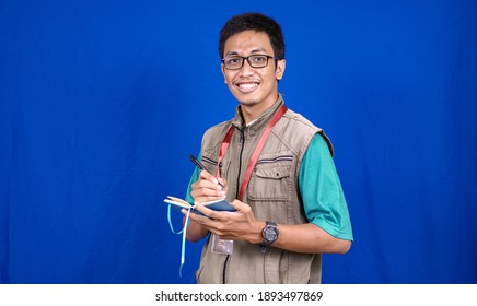 Asian Male Journalist Wearing Vest And Ready Writing For News Isolated On Blue Background 