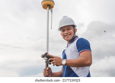 An Asian Male Land Surveyor Operating A GNSS Receiver. Using RTK Geodetic Surveying Equipment.