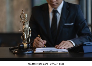 Asian male lawyer working with hammer and scales Goddess of justice, law enforcement officer, judge's hammer, as evidence of the case and documents taken into account, legal advisor online concept.