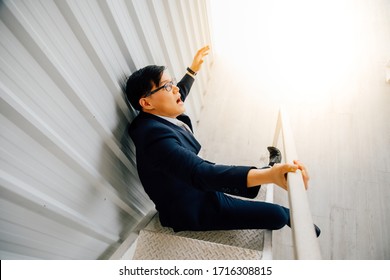 Asian Male Lying On Staircase After Slip And Fall Accident. Business Man Falling Down The Stairs In The Office. Accident And Insurance Injury Claim At Work