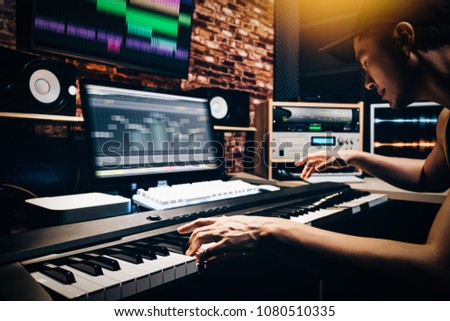 asian male music arranger hands composing song on midi piano & professional audio equipment in digital recording studio