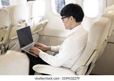 Asian Male Passenger In Airplane Use Computer Notebook Laptop And Wifi On Board, Young Asian Business Man Use Computer Laptop Traveling By Airplane Connecting Wifi.