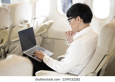 Asian Male Passenger In Airplane Use Computer Notebook Laptop And Wifi On Board, Young Asian Business Man Use Computer Laptop Traveling By Airplane Connecting Wifi.