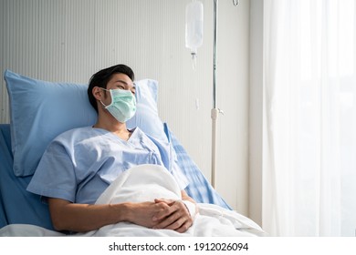 Asian Male Patient Lying On Bed With Face Mask In Recovery Room In Hospital Ward. All People Wearing Mask To Prevent Covid19 Virus Infection During Coronavirus Pandemic. The Man Feels Lonely And Bore.