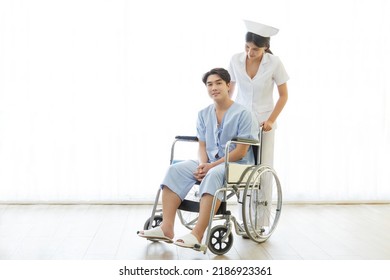 Asian Male Patient Sitting On Wheelchair While Nurse Supporting At Hospital Ward. Caregiver Therapist Nurse Support  Male Patient  Sitting On Wheelchair. Medical Therapy Insurance Concept.