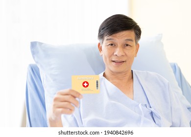 Asian Male Patients Smile And Showing Health Card For Medical Expenses On A Hospital Bed. Elderly Health Insurance, Life Insurance And Financial Planning