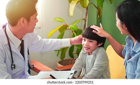 Asian Male Pediatrician Talking Exam With Child Boy Patient Visit Doctor And Young Asian Mother. Professional, Consulting Pediatric Health Checkup In Clinic Office. Medical Health Care Concept.