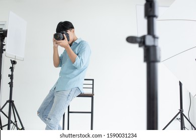 An Asian Male Photographer Took A Photo In The Studio And Sit On The Chair With Studio Lights As A Backdrop And Copy Space.