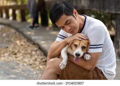 Asian Male Playing And Hugging With Pet Dog. Young Man Spending Some Time With His Dog In The Park. Asian Man Having Fun With His Dog