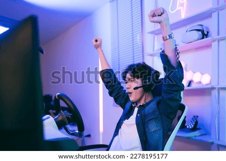 Asian male pro gamer playing an online car drive simulation game with steering wheel controller. Gamer winning an esports game with victory emotion. The player rejoices in victory in the competition.