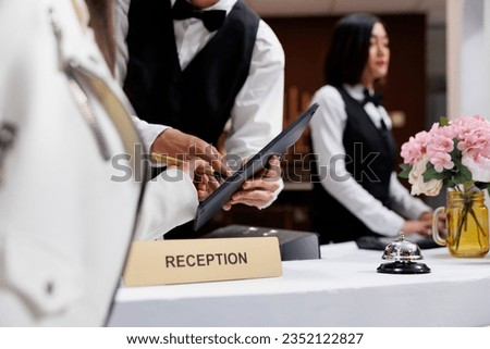 Asian male receptionist at contemporary hotel helps customer sign registration form. Booking hotel room at luxurious resort by going through visitor registry at front desk 商業照片 © 