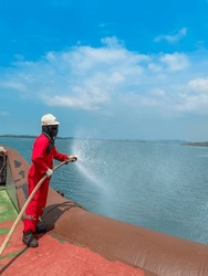 An Asian Male Sailor Wearing Coverall Is Testing The Fire Hose During The Annual Inspection At The Stern Of A Supply Ship. Tested Of Fire Hydrant For Fire Fighting Appliance