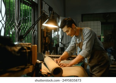 Asian male shoemaker meticulously measuring and cutting a large piece of leather on workbench. - Powered by Shutterstock