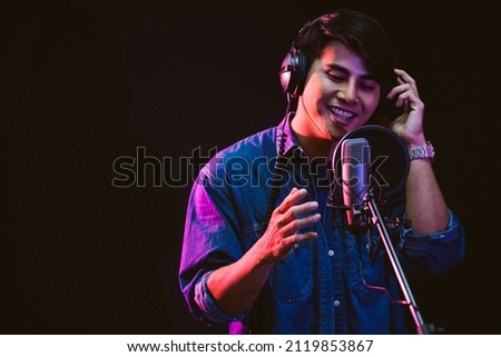 Asian male singer recording songs by using a studio microphone and pop shield on mic with passion in a music recording studio. Performance and show in the music business. Focus on male face