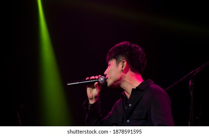 An Asian Male Singer Stands With A Microphone Singing Alone On Stage, With Beautiful Yellow Lights On The Stage.