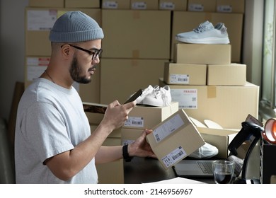 Asian male small business owner using mobile app on smartphone checking parcel box. Warehouse worker, seller holding phone scanning retail drop shipping package postal parcel bar code. - Shutterstock ID 2146956967