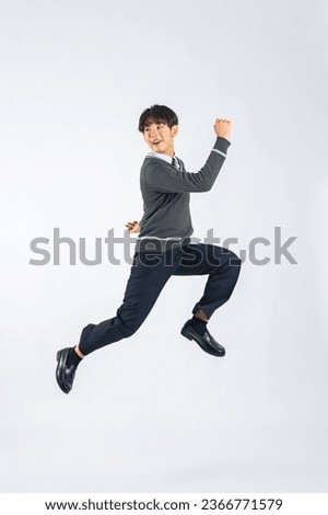 Asian male student jumping in a studio with a white background.