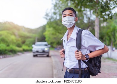 An Asian Male Student In White High School Uniforms Wearing The Mask Stand On The Side Of The Road Waiting For Car To Go Back Home After School During The Coronavirus 2019 (Covid-19) Epidemic.