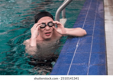 Asian male swimmer adjusting swim goggles in pool - Powered by Shutterstock