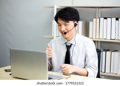 Asian Male Teacher Or Tutor Wearing A Headset, He Was Teaching Students Via Video Conferencing System On A Laptop From Home. The Young Man Is Meeting With Colleagues At The Webinar.