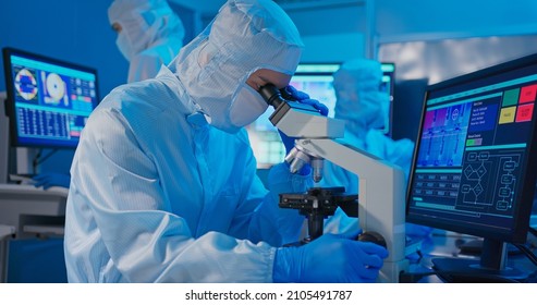 Asian Male Technician In Clean Room Suit Work At Semiconductor Manufacturing Plant By Microsope