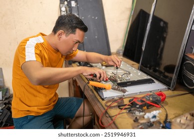 Asian male technician removing electronic circuitry while working at a service station - Powered by Shutterstock