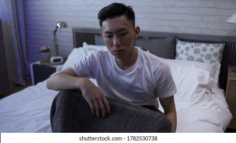 Asian Male Tossing And Turning On Bed Is Having A Disturbed Sleep. Closeup Japanese Guy Waking Up From A Nightmare Is Sitting And Mopping The Sweat From His Brow. 