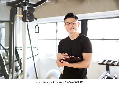 Asian Male Trainer Standing With A Smile In The Training Gym