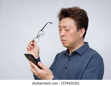 Asian Male Trying To Read Something On His Mobile Phone. Poor Sight, Presbyopia, Myopia.