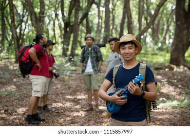 Asian Male With Ukulele Hiking To The Forest With Friends