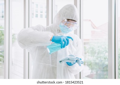 Asian Male Wear PPE Protective Suit Use Alcohol Sanitizer Wipe Cleaning Inside A Building Or Office,To Prevent Spread Of Disease From Crisis Of Coronavirus (COVID‑19) Outbreak.New Normal Concept.