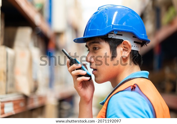 Asian male worker working with communication\
radio in automotive spare parts warehouse. people, car service,\
repair and maintenance\
concept