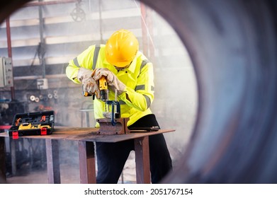 Asian male workers at an industrial factory wear green work clothes and goggles to prevent metal chips from penetrating. Use an industrial metal drill to drill metal.