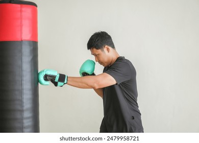 Asian man athlete wearing boxing gloves practicing boxing with a focus and determination intensely punching a heavy punching bag, workout, exercise, sports fitness and martial arts training at gym - Powered by Shutterstock