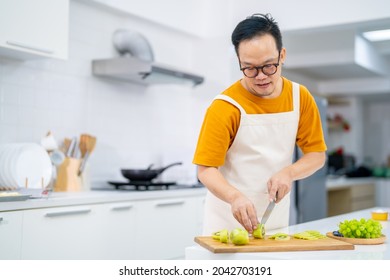 Asian Man Bakery Shop Owner Preparing Bakery In The Kitchen. Adult Male Using Kitchen Knife Cut Fresh Fruit For Making Fruit Tart. Small Business Entrepreneur And Indoor Lifestyle Baking Concept.