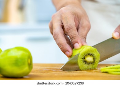 Asian Man Bakery Shop Owner Preparing Bakery In The Kitchen. Adult Male Using Kitchen Knife Cut Fresh Fruit For Making Fruit Tart. Small Business Entrepreneur And Indoor Lifestyle Baking Concept.