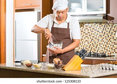 Asian Man Baking Homemade Cake In His Kitchen For Dessert