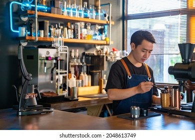 Asian Man Barista Using Coffee Grinder Machine Grinding Roasted Coffee Beans At Cafe. Male Coffee Shop Owner Brewing Black Coffee Serving To Customer. Small Business Restaurant Food And Drink Concept