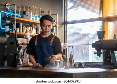 Asian Man Barista Using Towel Sweeping Counter Bar With Alcohol Sanitizer Before Opening Cafe. Male Coffee Shop Owner Cleaning Up Table For Service To Customer. Small Business Owner Working Concept